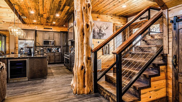Un interior rústico con vigas de madera, un pilar central de madera, una escalera y una zona de cocina.