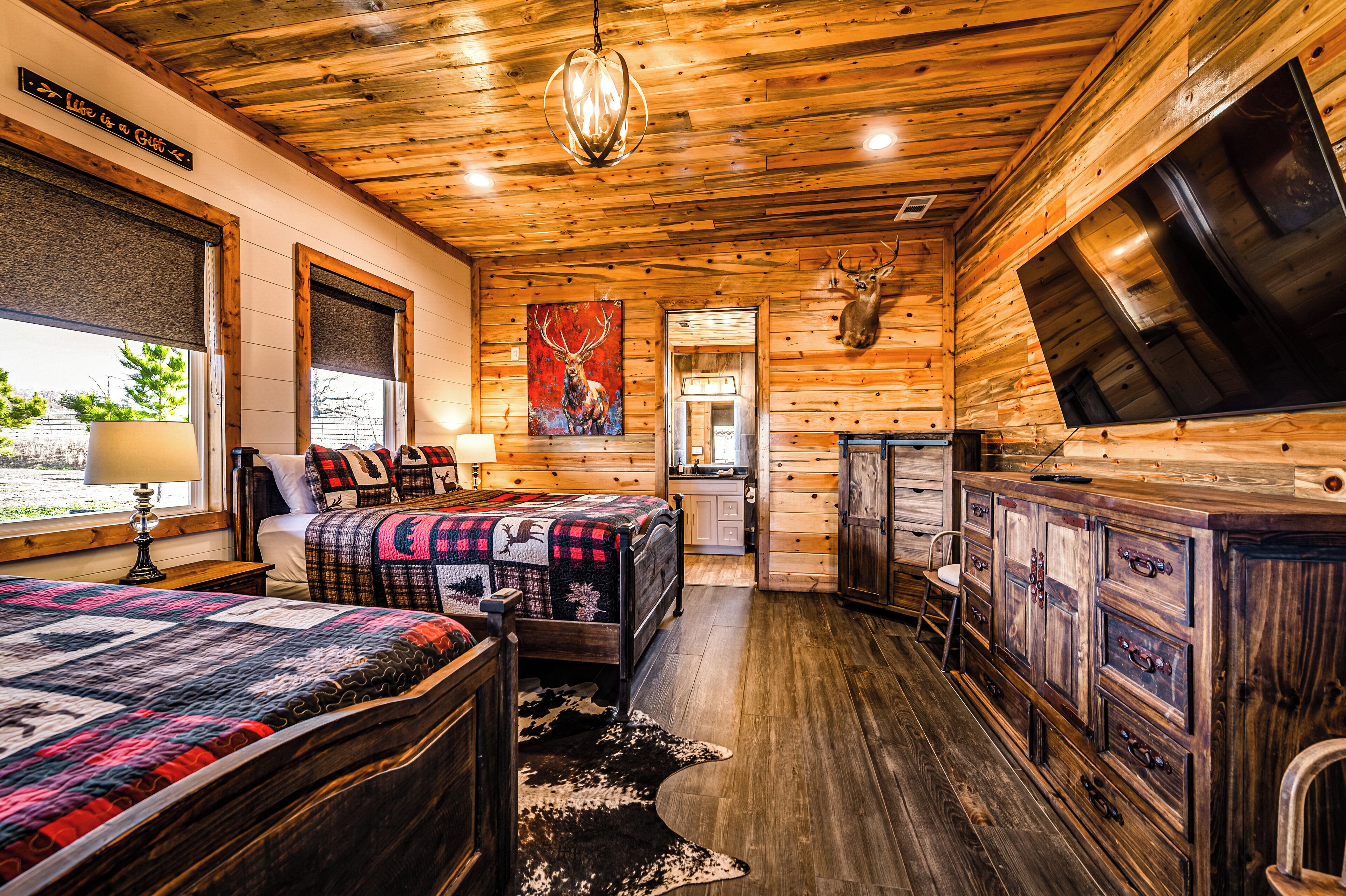 A log cabin-style bedroom with a large bed, a dresser, and a mounted deer head.