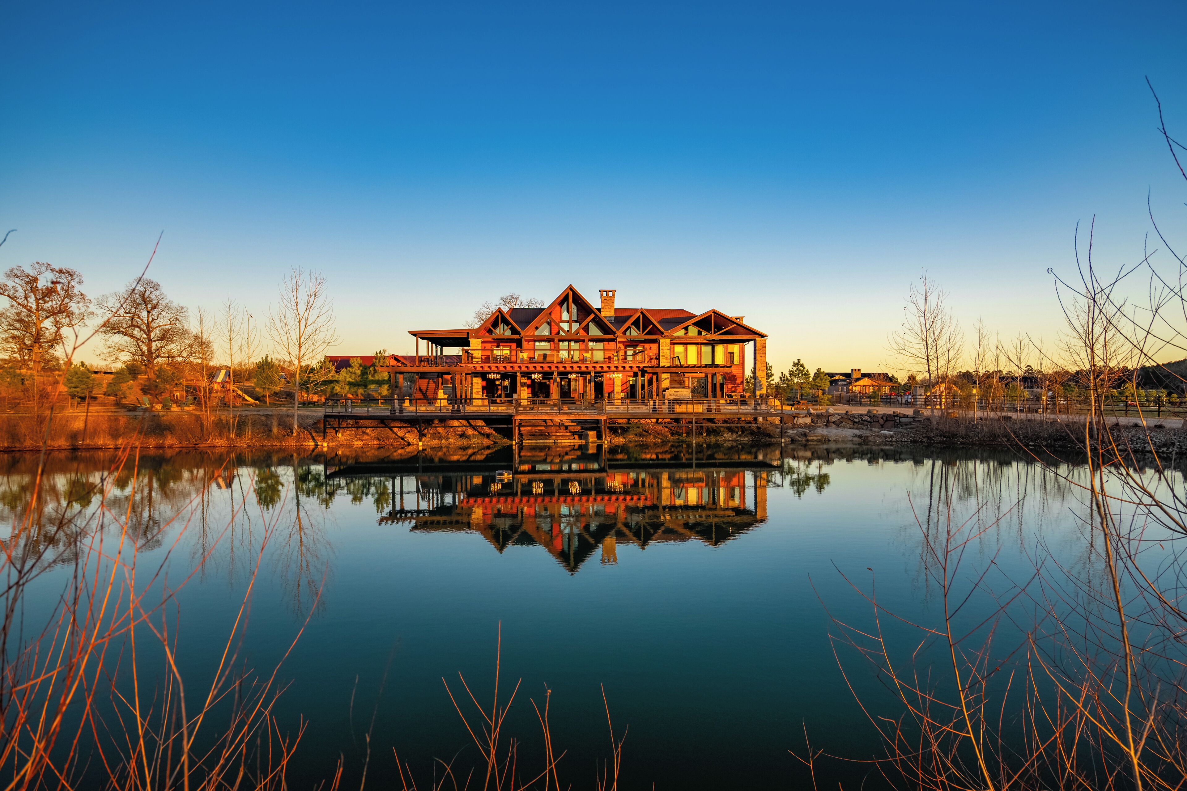 A large, multi-story house with a prominent chimney, reflecting in a calm body of water.
