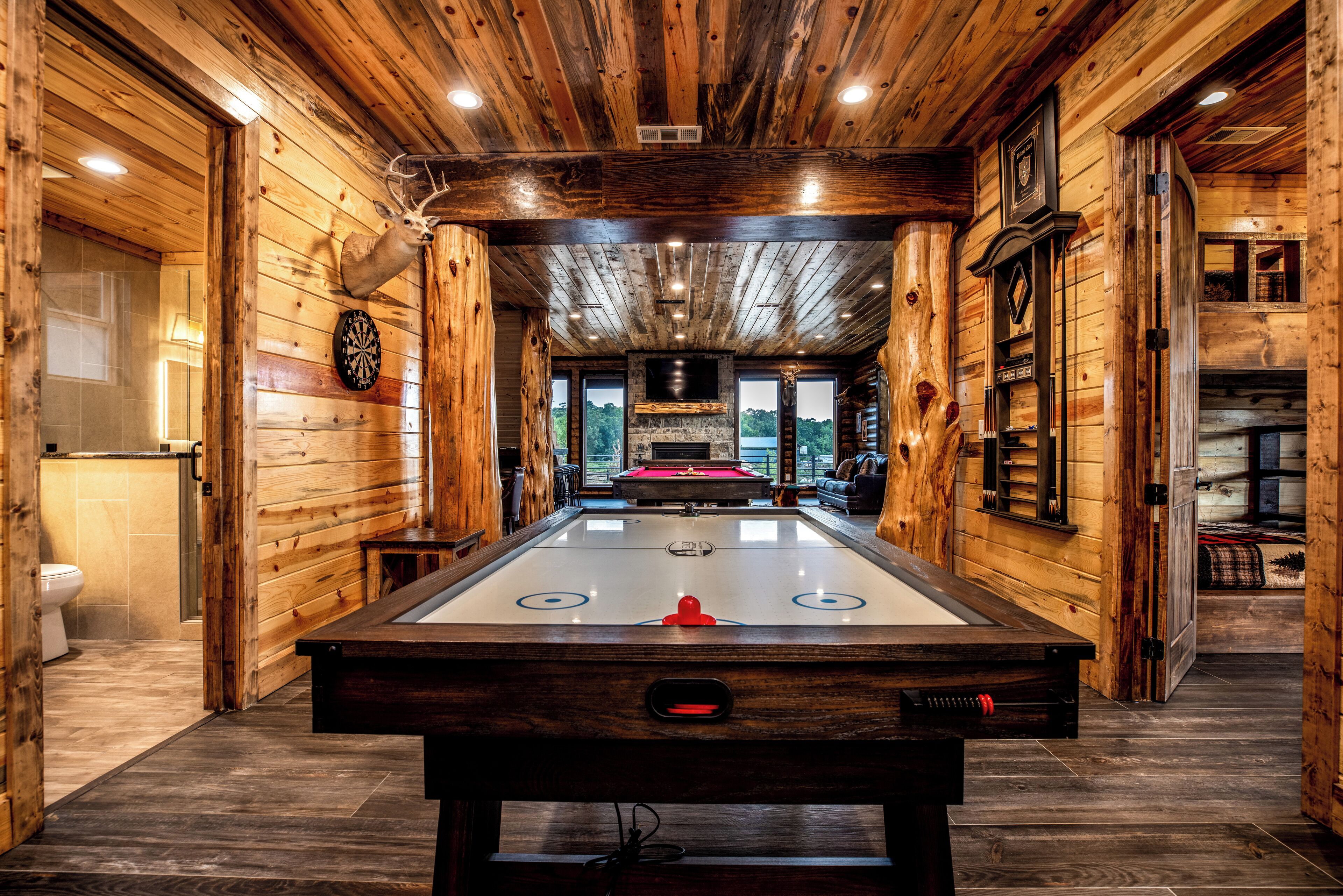 A wooden-floored room with a pool table, a dartboard, and a mounted deer head.