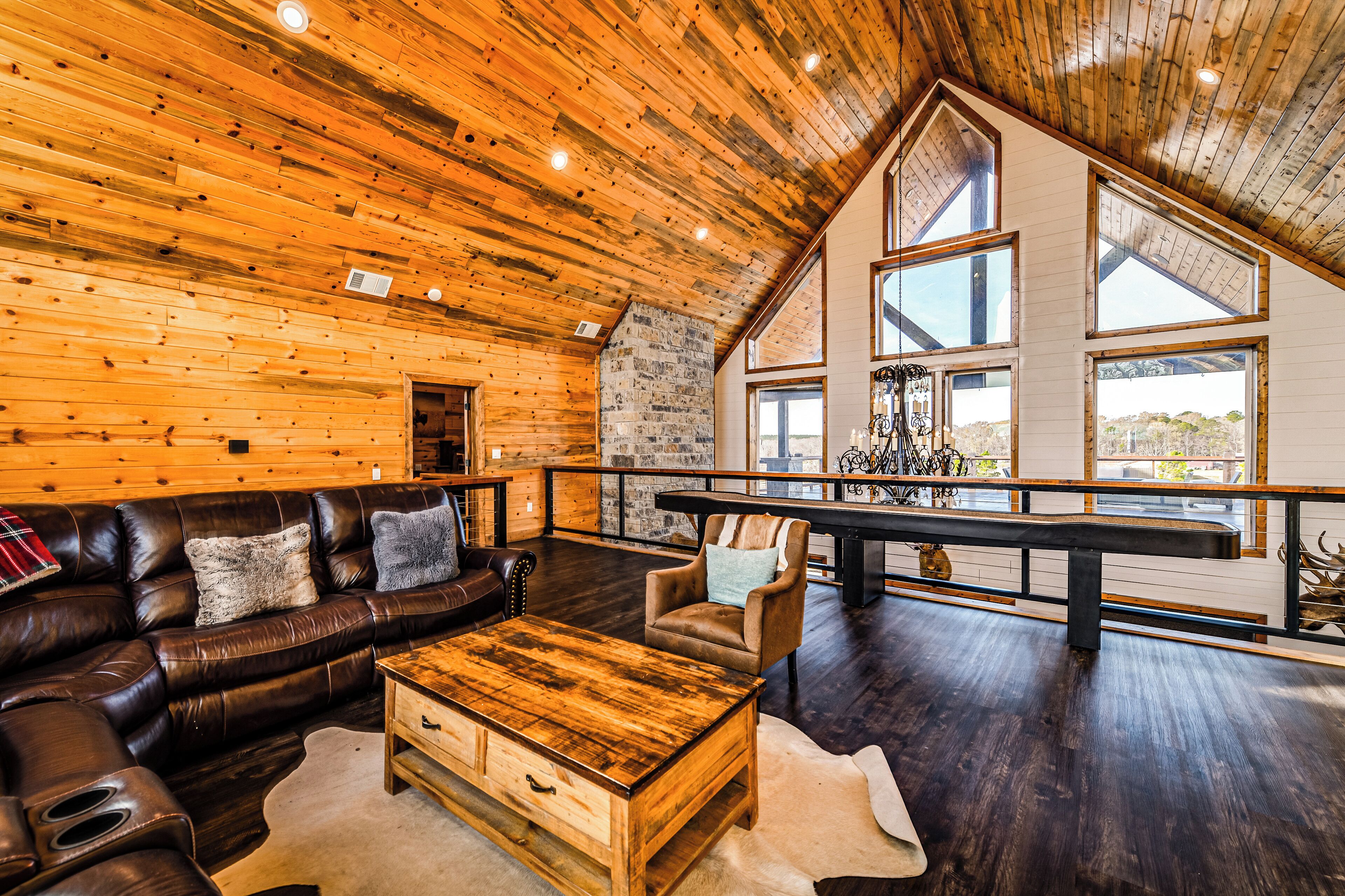 A spacious living area with a wooden ceiling, leather sofa, and a large window overlooking a scenic view.