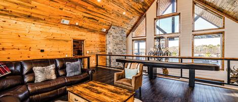 A spacious living area with a wooden ceiling, leather sofa, and a large window overlooking a scenic view.