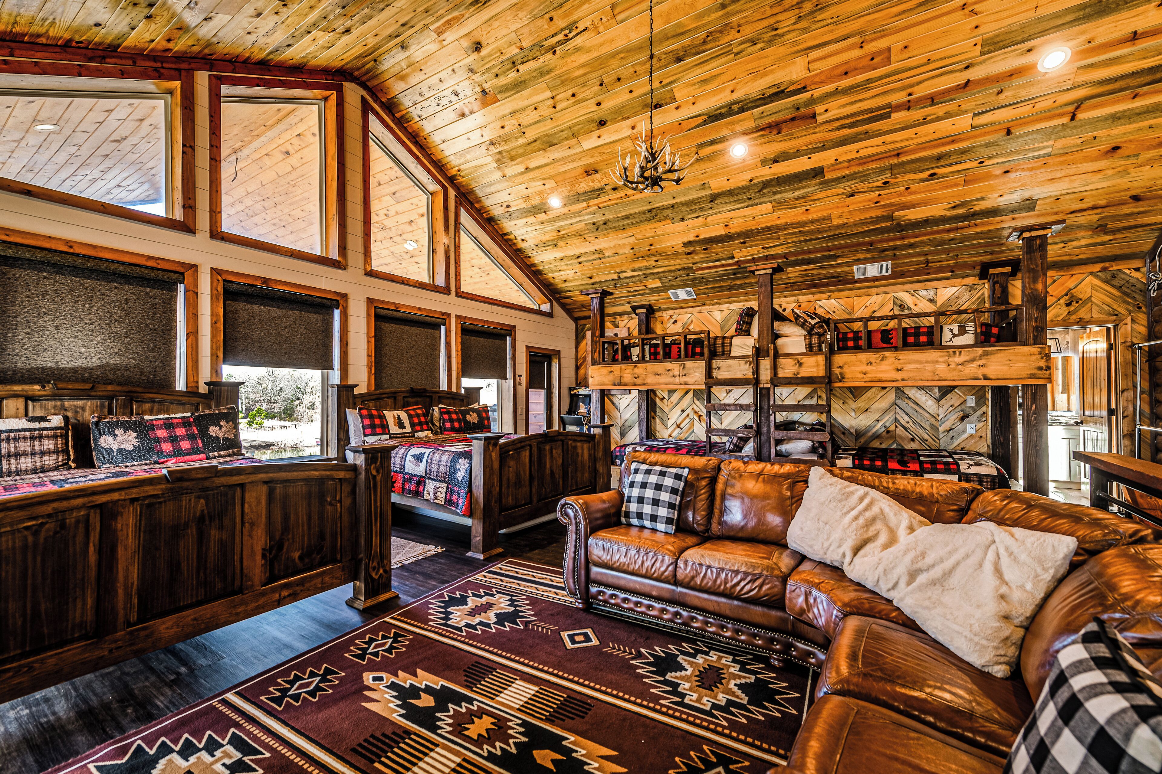 A rustic interior with a wooden ceiling, large windows, a leather sofa, and a herringbone-patterned wall.
