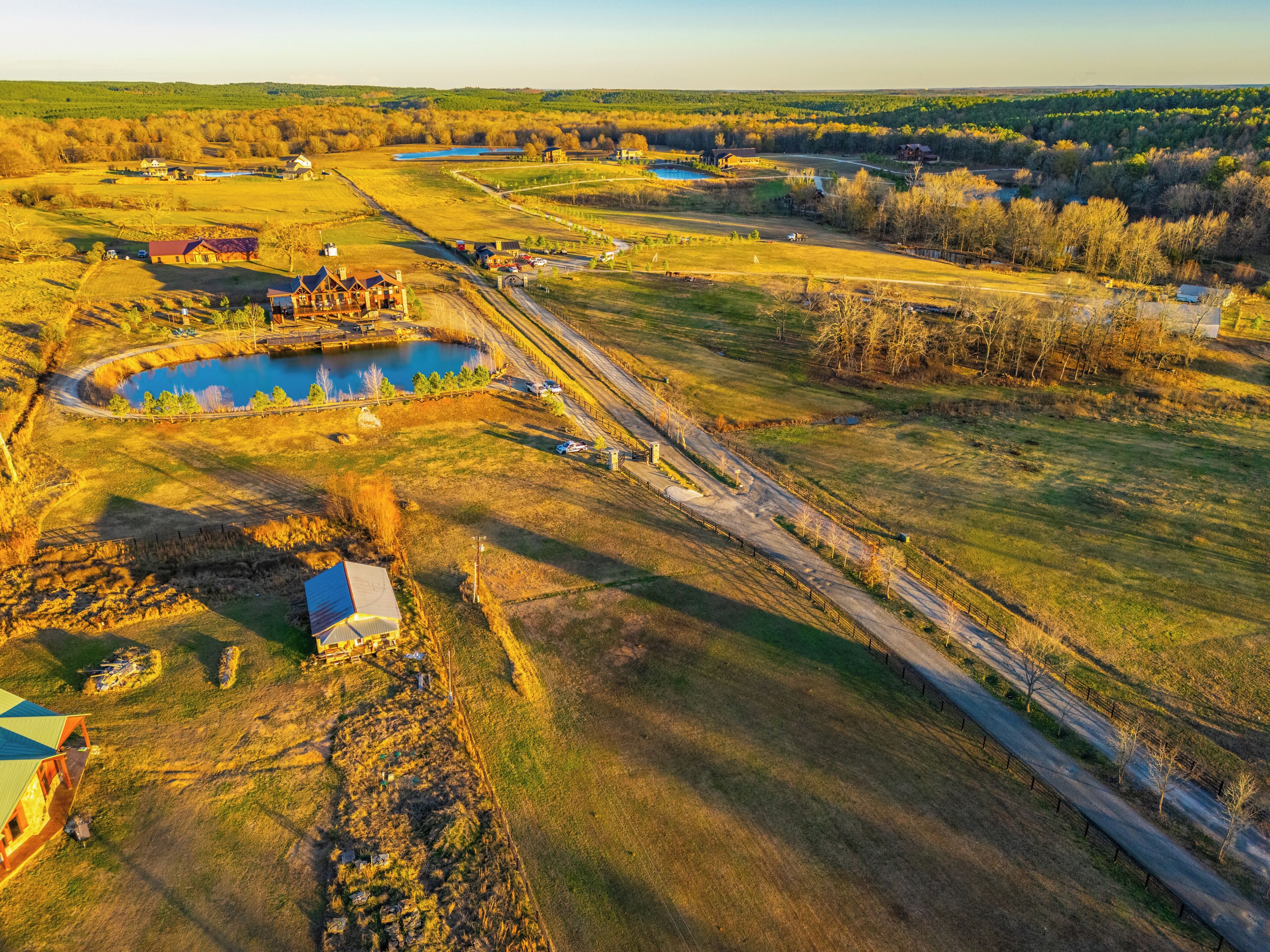 An aerial view of a rural landscape with a large pond, several buildings, and a winding road.