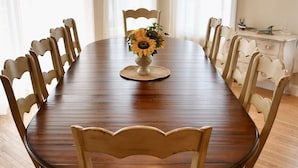 Une salle à manger avec une table et des chaises en bois, un vase rempli de fleurs et un lustre.