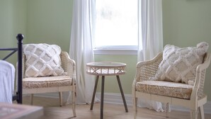A room with two wicker chairs with patterned cushions, a small round table, and a window with white curtains.