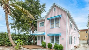 A two-story pink house with a blue awning, a covered porch, and a number '1703' on the side.