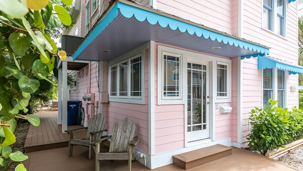 A pink house with a porch, a wooden chair, and a blue trash bin.