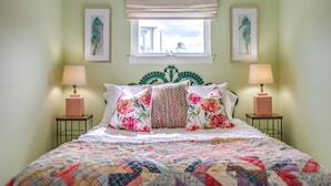 A bed with a floral quilt, two bedside lamps, and a window with a view of a building.