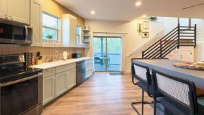 A modern kitchen with stainless steel appliances, a dining area with a bar, and a staircase leading to an upper level. - Rooftop Jungle with Skyline Views (Austin)