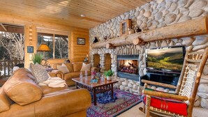 A cozy log cabin interior with a stone fireplace, leather sofa, and a television. - Abode at Black Bear #305, hot tub, pool & gym, Silver Lake village (Park City)