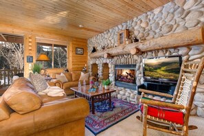 A cozy log cabin interior with a stone fireplace, leather sofa, and a television.