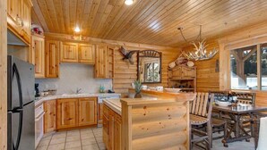 A log cabin interior with wooden cabinets, a kitchen island, a dining area with wooden chairs, and a large window. - Abode at Black Bear #305, hot tub, pool & gym, Silver Lake village (Park City)