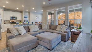 A modern kitchen with white cabinets and a microwave, a large L-shaped sectional sofa with multiple cushions, and a dining area with a table and chairs. - Escondido 2275, Sleeps 20, Ping Pong Table, BBQ - near Sand Hollow, and Quail Creek (Washington)