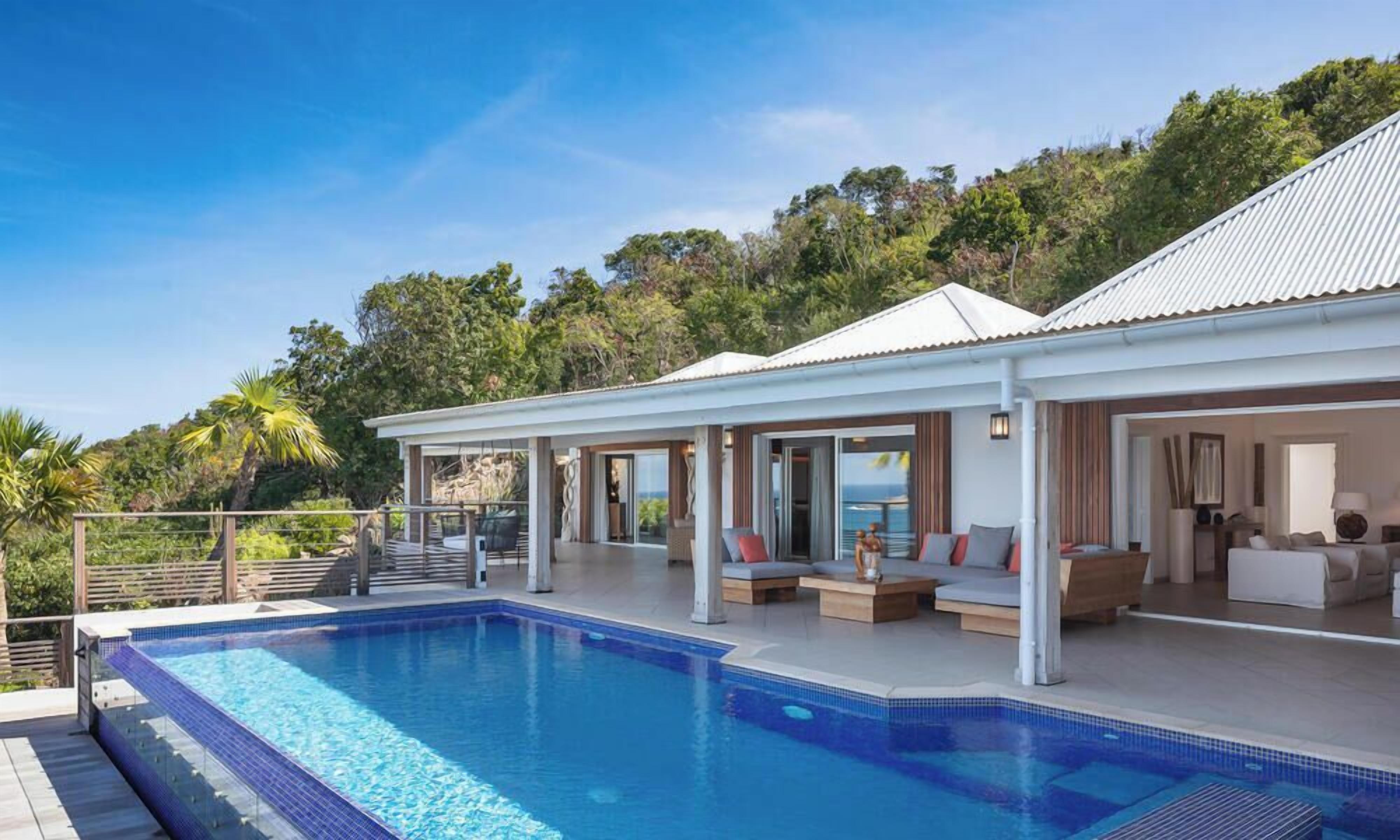 Una villa moderna con piscina, mobiliario exterior y vistas del paisaje circundante.
