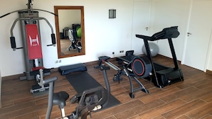 Uma academia em casa com esteira, bicicleta ergométrica e aparelho de musculação.
