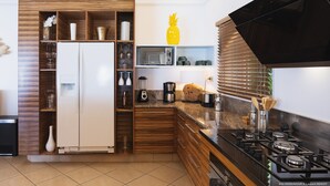 Eine moderne Küche mit Einbaukühlschrank, Mikrowelle und Gaskochfeld. Holzregale beherbergen Küchenutensilien und eine dekorative Ananas.