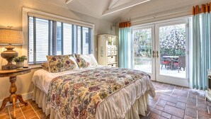 Una camera da letto con un letto grande, un comodino, una lampada, una finestra con persiane, un armadio e una porta scorrevole in vetro che dà su uno spazio esterno.