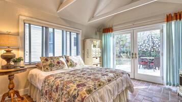 Une chambre avec un grand lit, une table de chevet, une lampe, une fenêtre avec des stores, une armoire et une porte-fenêtre coulissante donnant sur un espace extérieur.