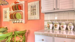 Una cucina con mobili bianchi, una sedia verde e uno scaffale con piatti.