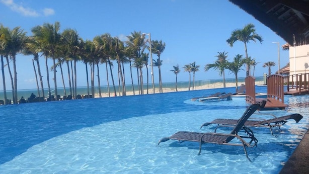 Une piscine d’un bleu éclatant, avec des chaises longues, des palmiers et une plage en arrière-plan.