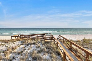 A wooden boardwalk leading to a beach with a clear view of the ocean.