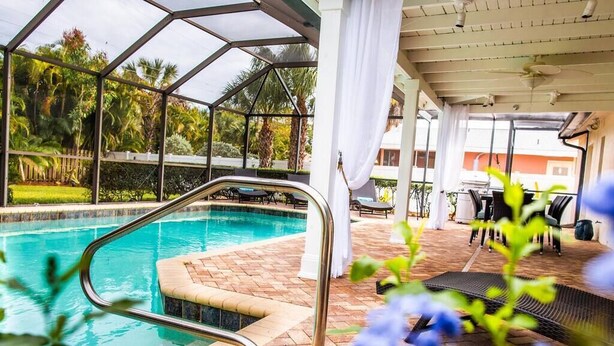 Una piscina con cerramiento de vidrio, rodeada de un patio con mobiliario exterior.