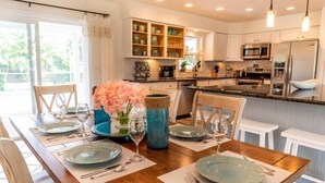 Una cocina moderna con armarios blancos, electrodomésticos de acero inoxidable y un comedor con mesa de madera para cuatro.