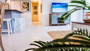 Una sala de estar moderna con televisor, muebles blancos y una planta.