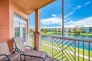 A balcony with two chairs, a view of a swimming pool, and a building with multiple windows in the background. - Atlantis 204B (St. Augustine Beach)