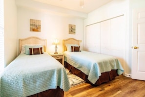 A room with two beds, a nightstand with a lamp, and a white door. - Atlantis 204B (St. Augustine Beach)