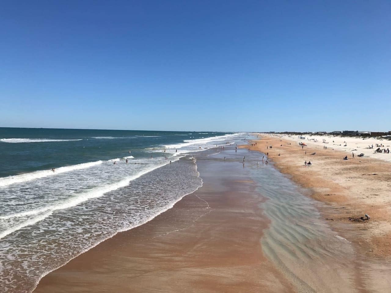 A beach with a wide sandy shore, gentle waves, and a clear blue sky.