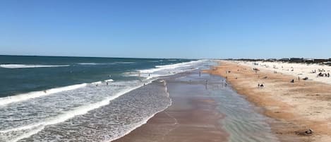 A beach with a wide sandy shore, gentle waves, and a clear blue sky.