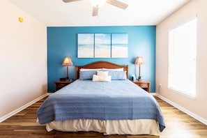 A bedroom with a large bed, two bedside tables with lamps, a ceiling fan, and a window with blinds. - Atlantis 204B (St. Augustine Beach)