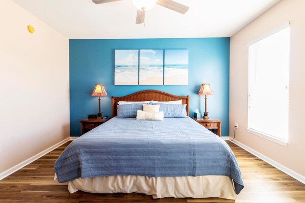 A bedroom with a large bed, two bedside tables with lamps, a ceiling fan, and a window with blinds.