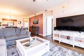 A living room with a grey sofa, a white coffee table, a flat-screen TV, and a cabinet with decorative items. - Atlantis 204B (St. Augustine Beach)