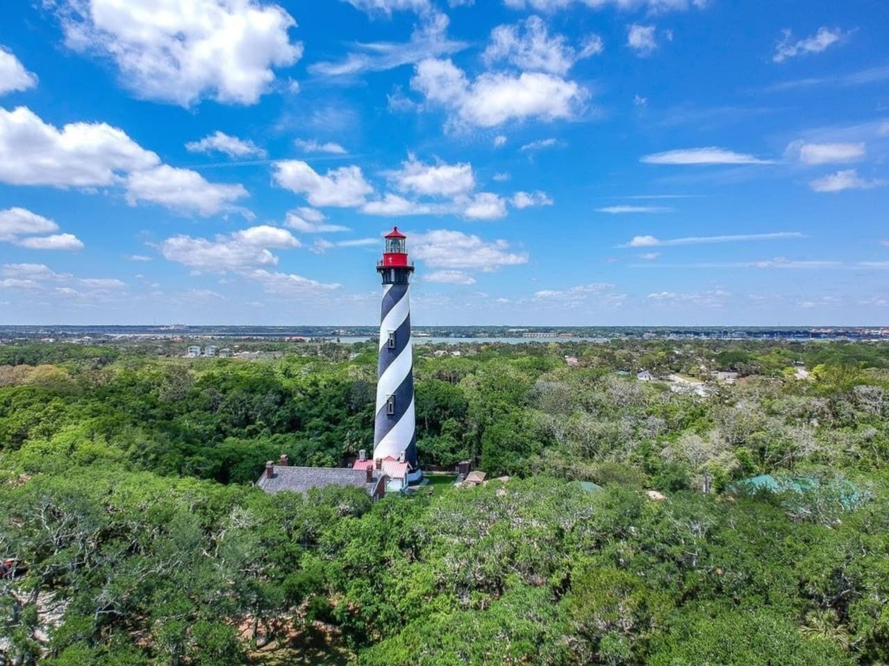 A lighthouse with a striped pattern, surrounded by dense greenery and a clear sky.