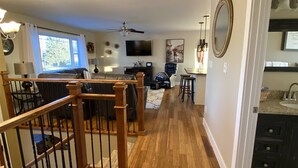 Un salón espacioso con una escalera de madera, televisor y zona de comedor.