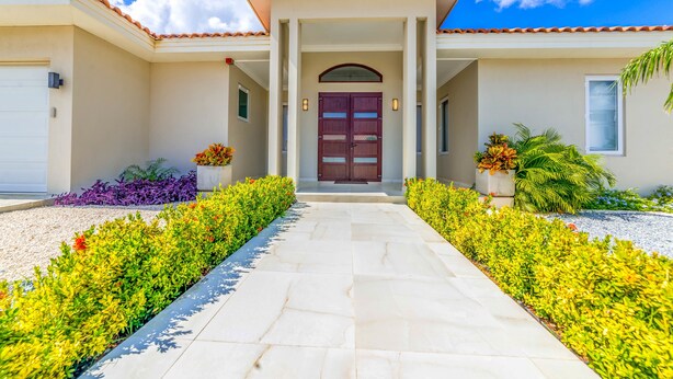 Une maison avec un toit en tuiles, une entrée centrale dotée d’une double porte et un chemin menant à l’entrée.