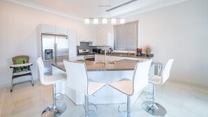 Une cuisine moderne avec un îlot central, des tabourets de bar blancs et une chaise haute.