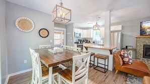 A modern kitchen with white cabinets, a wooden dining table, and a stone fireplace. - Hygge Blue Chalet ~ 2 Large Suites, Sleeps 8, Hot Tub, Convenient, 2 balconies (Sevierville)