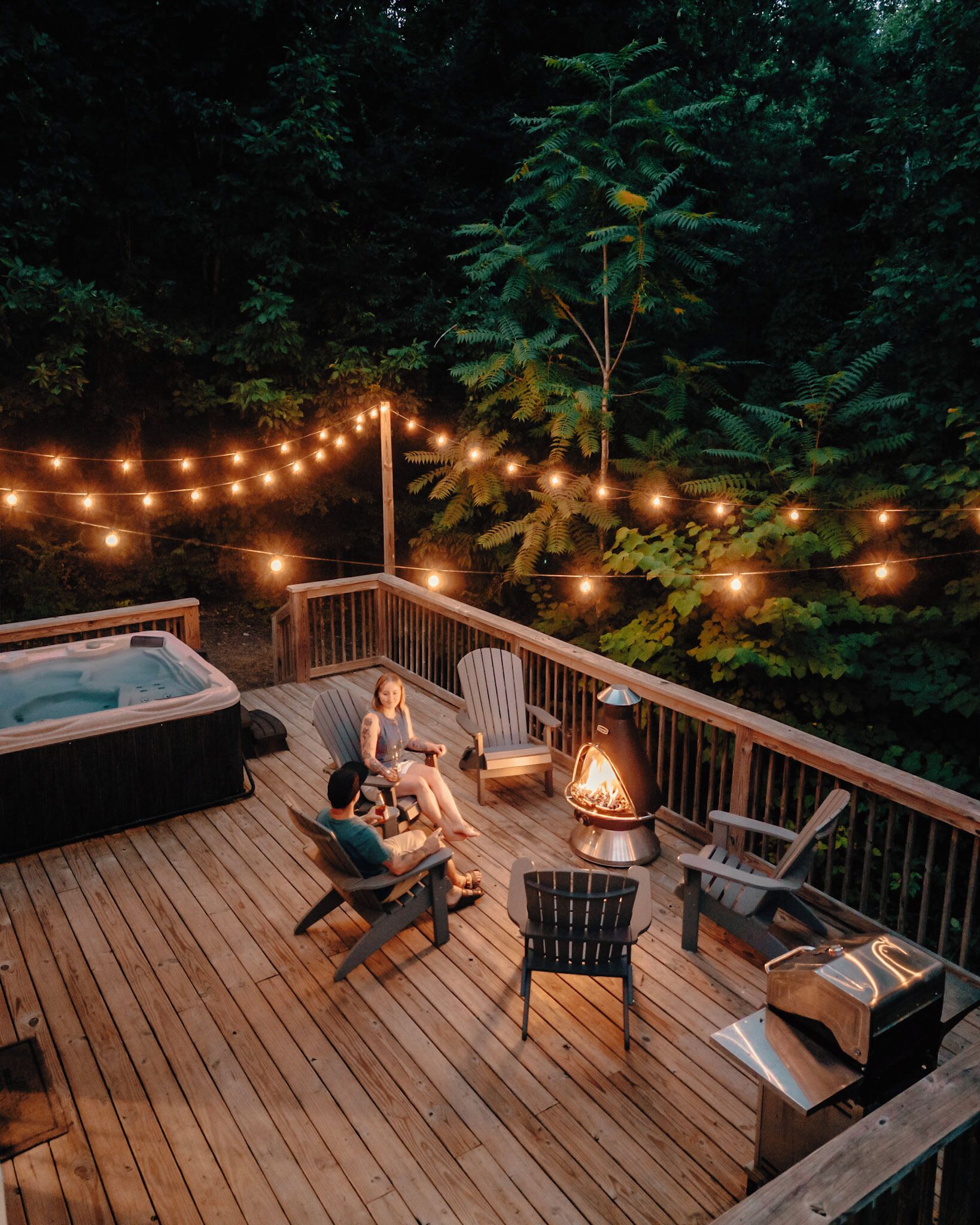 Una terraza de madera con mobiliario exterior, un jacuzzi y un pozo de fuego.