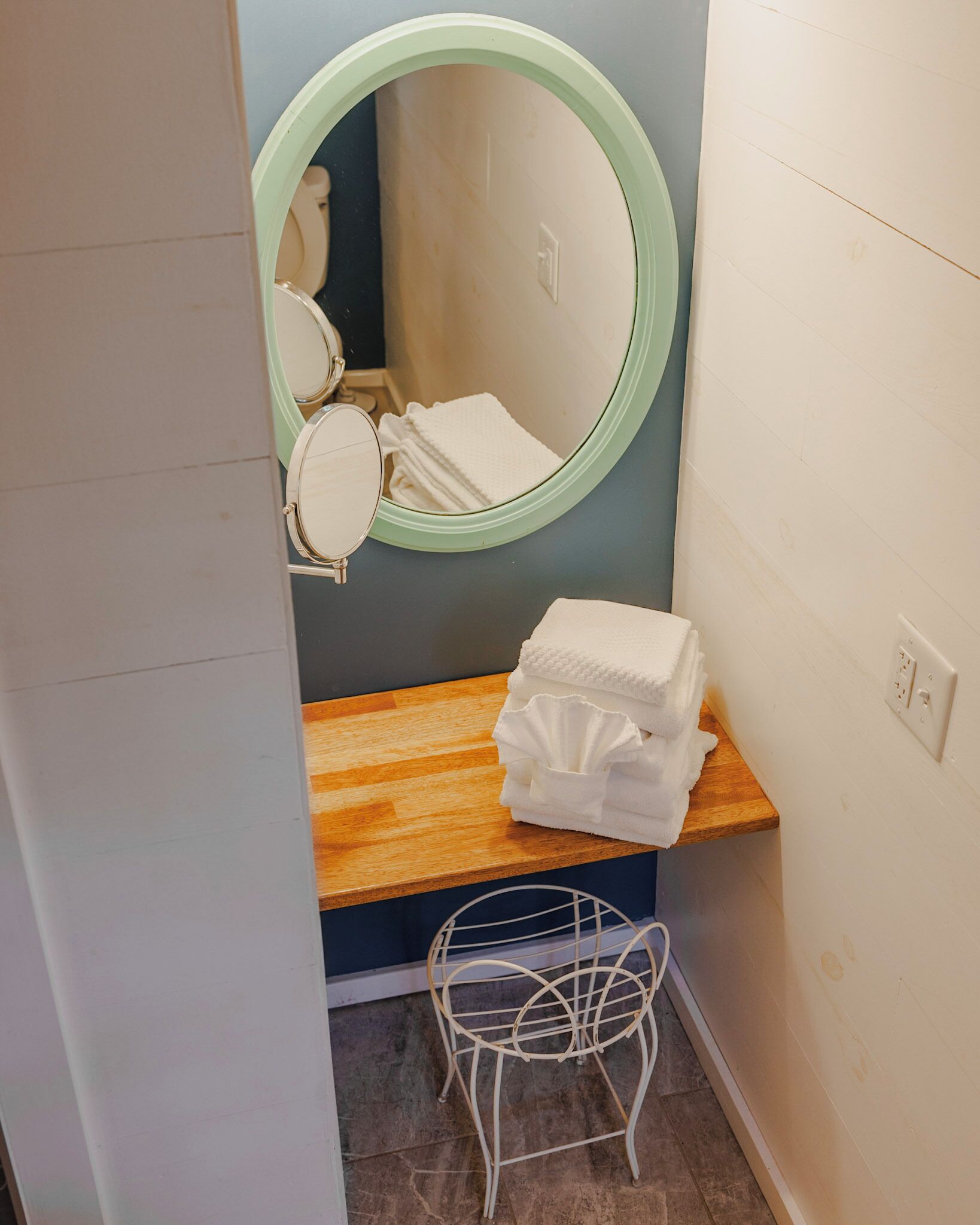 Ein Badezimmer mit einem hölzernen Waschtisch, einem runden Spiegel und einem Stapel weißer Handtücher.