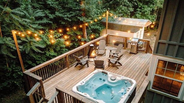 A deck with a hot tub, wooden chairs, and a barbecue area surrounded by trees and string lights. - Hygge Blue Chalet ~ 2 Large Suites, Sleeps 8, Hot Tub, Convenient, 2 balconies (Sevierville)