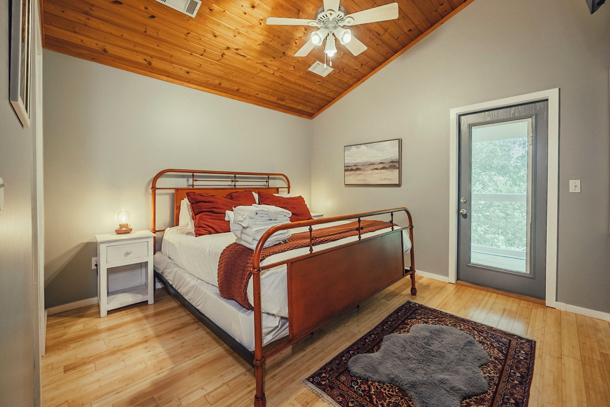 Un dormitorio con techo de madera, estructura de cama metálica, mesita de noche, alfombra y puerta con vistas.