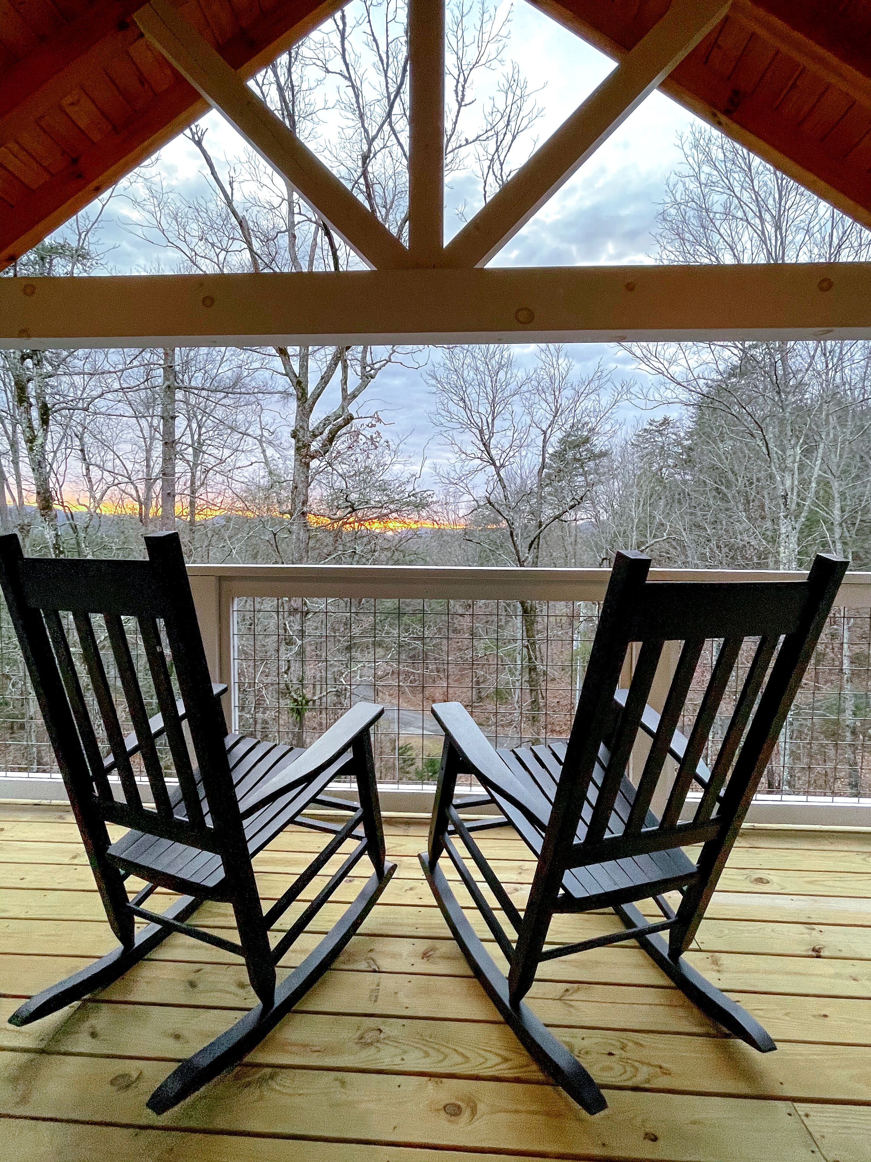 A wooden deck with two rocking chairs facing a metal railing.