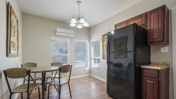 A kitchen with a black refrigerator, wooden cabinets, a dining table with chairs, and a hanging light fixture. - WL1- Modern 2BR Retreat Minutes from Downtown & Top SA Attractions (San Antonio)