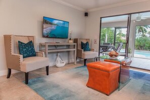 Een woonkamer met twee fauteuils, een glazen salontafel, een flatscreen televisie en uitzicht op een zwembad.