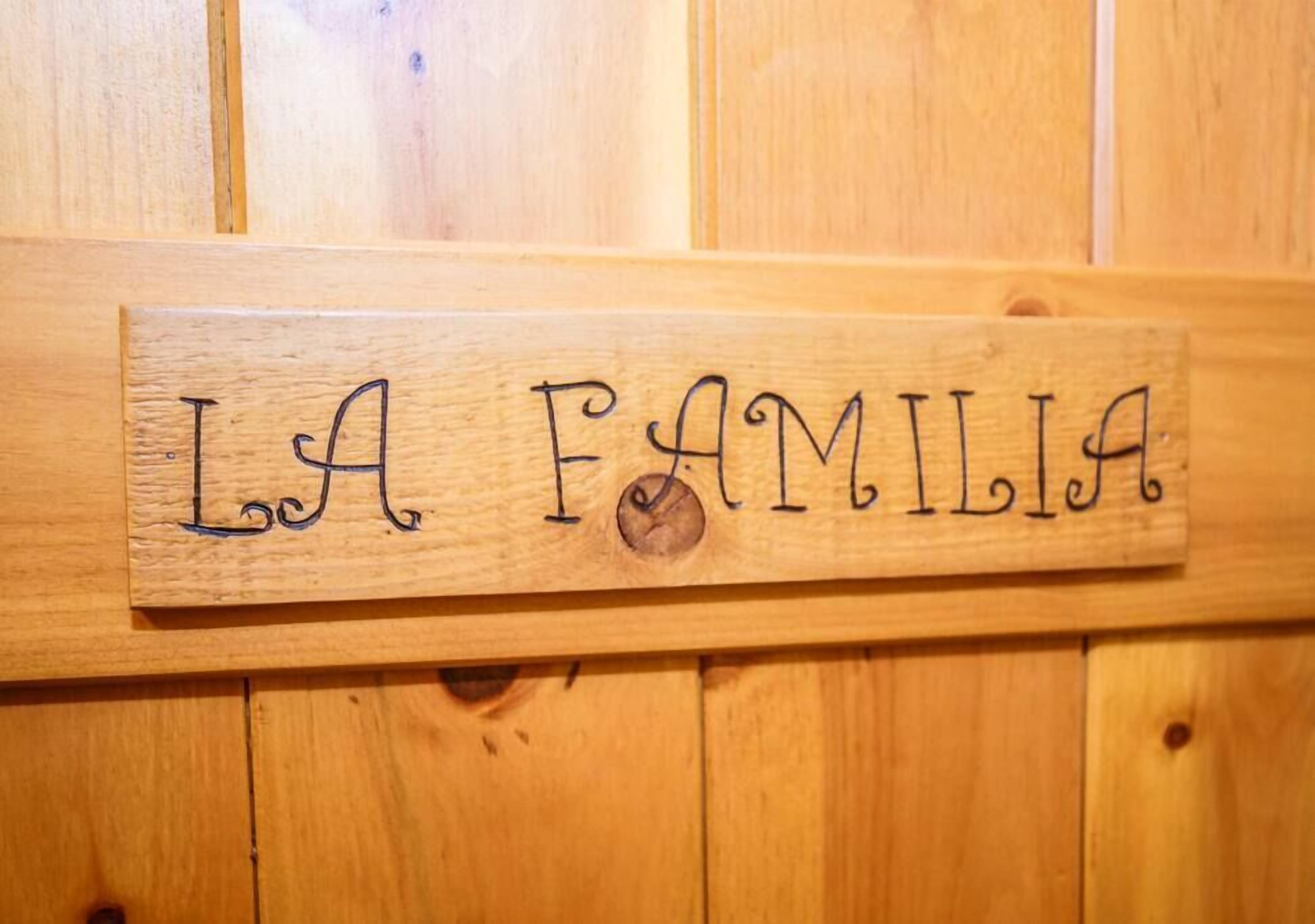 A wooden plaque with the words "LA FAMILIA" written on it, mounted on a wooden wall.