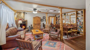 A cozy living room with a fireplace, leather sofa, wooden furniture, and a bookshelf. - Encanto Lodge - Downtown Chama 1 Block From Train (Chama)